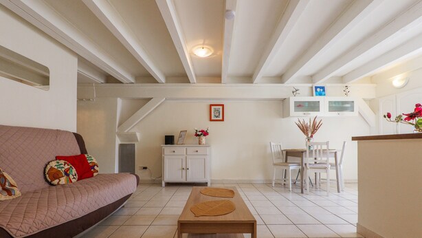 A living room with a sofa, a wooden coffee table, a dining area with a table and chairs, and a kitchen area with cabinets and a countertop. - Charming One-Bedroom Apartment in the Heart of Vals-les-Bains (Vals-les-Bains)