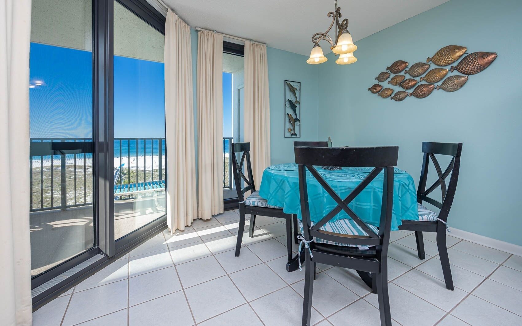A balcony with a view of the beach, a dining table with chairs, and a chandelier.