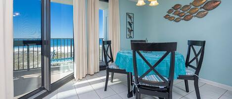 A balcony with a view of the beach, a dining table with chairs, and a chandelier.