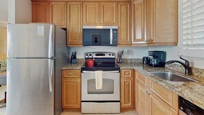 Eine Küche mit Holzausstattung, einem Edelstahlkühlschrank, einer Mikrowelle, einem Backofen und einer Arbeitsplatte aus Granit.