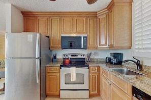 A kitchen with wooden cabinets, a stainless steel refrigerator, a microwave, an oven, and a granite countertop. - Cozy studio with shared pool, panoramic views, and internet (Bonita Springs)