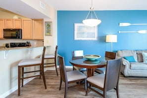 A modern kitchen with wooden cabinets, a microwave, and a dining area with a round table and chairs. - 2BR~ Lagoon Pool~ Palms of Destin 21211 (Destin)