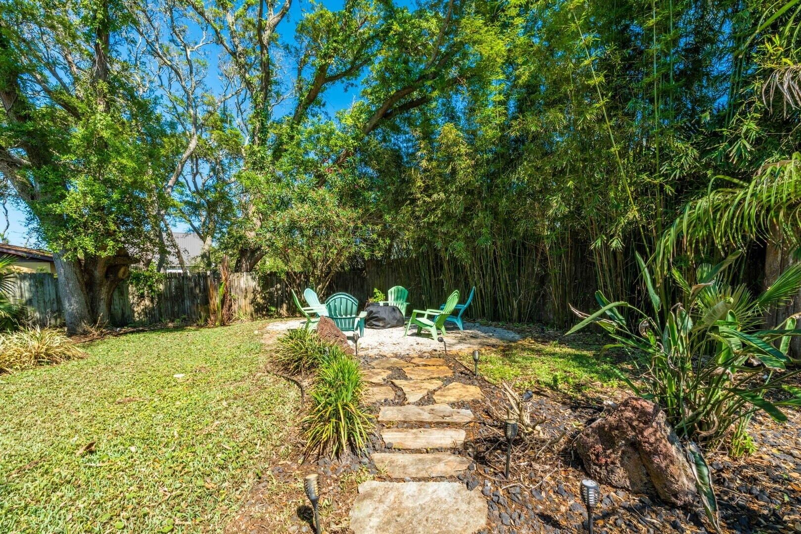 A backyard with a stone pathway, green chairs, and a large tree.