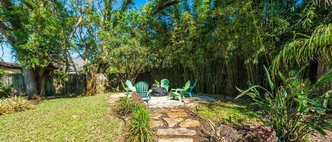 A backyard with a stone pathway, green chairs, and a large tree.