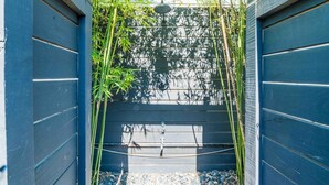 A narrow outdoor corridor with bamboo plants, a water feature, and a metal gate. - Vilano Beach I Ocean - Private Pool - Fire Pit 3 Bedroom Home (St. Augustine)