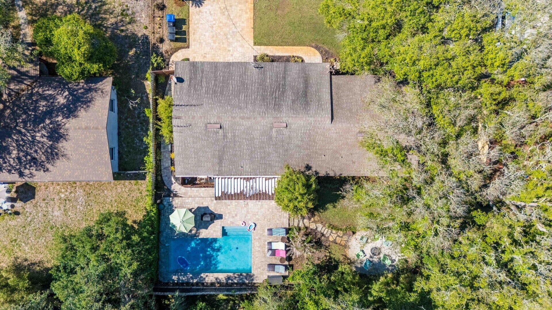 An aerial view of a house with a swimming pool, a covered patio, and surrounding greenery.