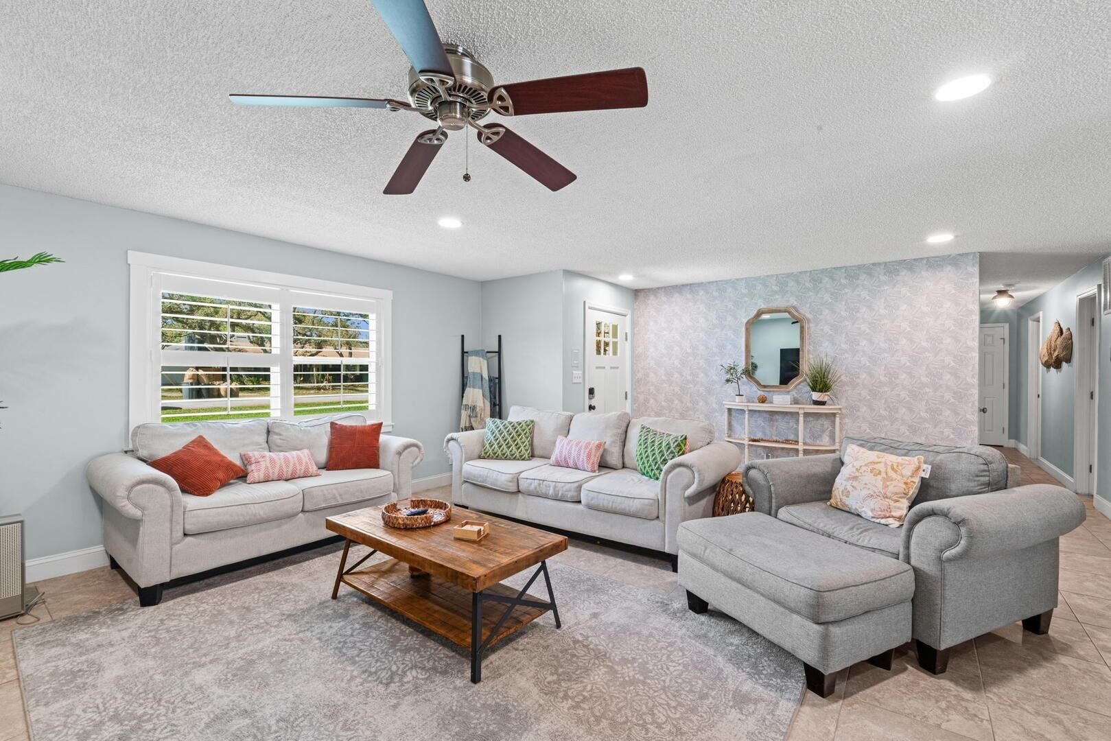 A living room with a ceiling fan, two sofas, a coffee table, and a window with blinds.