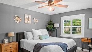 A bedroom with a bed, bedside table, lamp, and a window with a view. - Vilano Beach I Ocean - Private Pool - Fire Pit 3 Bedroom Home (St. Augustine)