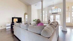 Ein geräumiges Wohnzimmer mit einer großen grauen Couch, einem Flachbildfernseher und einem Essbereich mit Tisch und Stühlen.