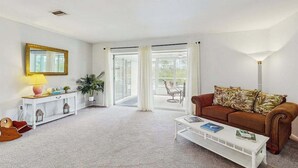 A living room with a white sofa, a coffee table, a lamp, a console table, and a large window with curtains. - Waterfront & ground-floor home with free WiFi, dock, pool, & central AC (Englewood)