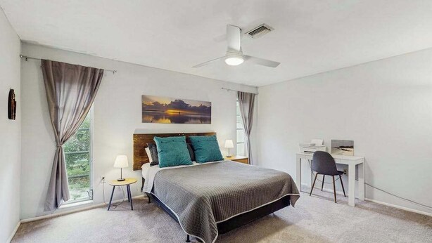 A bedroom with a bed, a desk, a chair, a ceiling fan, and a painting on the wall. - Waterfront & ground-floor home with free WiFi, dock, pool, & central AC (Englewood)