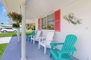 A covered porch with white and turquoise Adirondack chairs, a hanging flower basket, and a wall mural of sea turtles. - Waterfront home with canal views, patio, sun room, & central AC - near beach (Englewood)