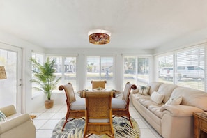A sunlit room with a dining table, chairs, a sofa, and a large window. - Waterfront home with canal views, patio, sun room, & central AC - near beach (Englewood)