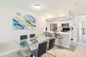 A modern kitchen with white cabinetry, stainless steel appliances, and a glass dining table with four chairs. - Centrally located duplex with on-site pool, firepit, patio, & BBQ - dog-friendly (Cape Coral)