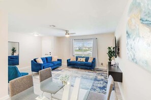 A living room with two blue sofas, a coffee table, and a TV. - Centrally located duplex with on-site pool, firepit, patio, & BBQ - dog-friendly (Cape Coral)