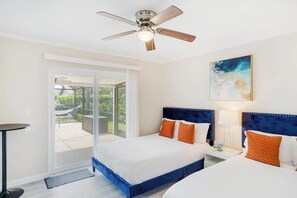A hotel room with two beds, a ceiling fan, a painting, and a view through a sliding glass door. - Centrally located duplex with on-site pool, firepit, patio, & BBQ - dog-friendly (Cape Coral)