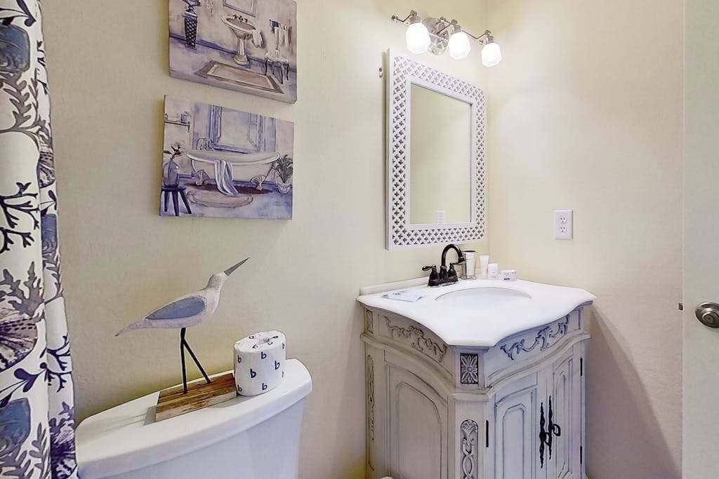 A bathroom with a toilet, sink, and mirror. There are two framed artworks on the wall.