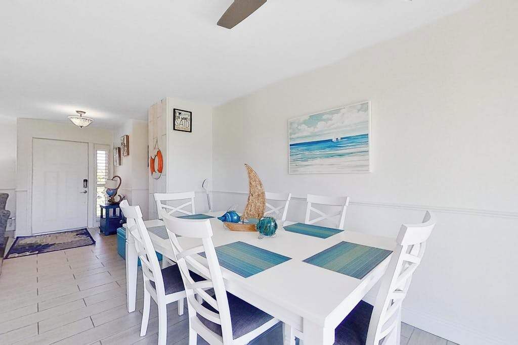 A dining area with a white table and chairs, a sailboat decoration, and a painting of a beach scene.