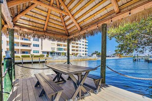 A wooden deck with picnic tables, a thatched roof structure, and a waterfront view. - Palms on the Canal | House in Cape Coral with direct water access (Cape Coral)