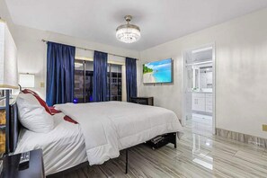 A hotel room with a bed, a television, a desk, and a bathroom visible through an open door. - Palms on the Canal | House in Cape Coral with direct water access (Cape Coral)