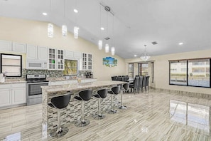A modern kitchen with white cabinets, a granite countertop, and a bar area with stools. - Palms on the Canal | House in Cape Coral with direct water access (Cape Coral)