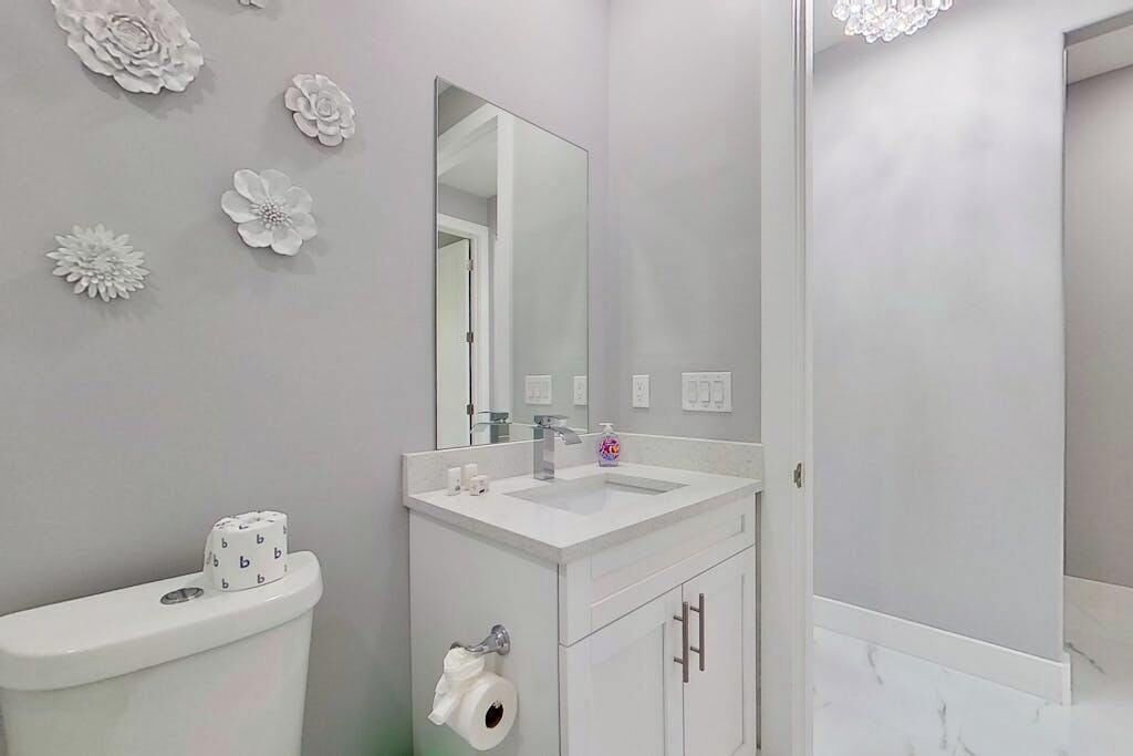 Une salle de bain équipée de toilettes, d’un lavabo, d’un miroir et agrémentée de fleurs décoratives sur le mur.