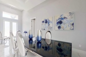 Ein moderner Essbereich mit einem schwarzen, spiegelnden Tisch, weißen Stühlen und abstrakter Wandkunst.