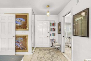 A hallway with white doors, a bookshelf, a small white bench, and a hanging light fixture. - Private Canal-Front Retreat with Pool, Lanai, Patio & Waterfront Deck (Cape Coral)