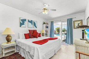 A bedroom with a bed, a ceiling fan, a window with curtains, a bookshelf, and a view of a pool. - Private Canal-Front Retreat with Pool, Lanai, Patio & Waterfront Deck (Cape Coral)