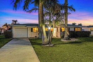 A residential house with a garage, palm trees, and a well-maintained lawn. - Private Canal-Front Retreat with Pool, Lanai, Patio & Waterfront Deck (Cape Coral)