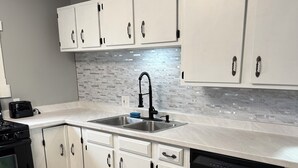 Una cucina moderna con mobili bianchi, un lavello in acciaio inossidabile, un rubinetto nero e una lavastoviglie.