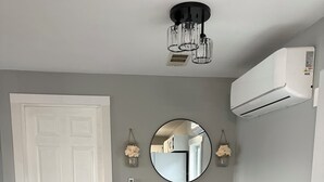 Zona pranzo con un tavolo rotondo, quattro sedie, un condizionatore d'aria a muro, un lampadario e una porta.