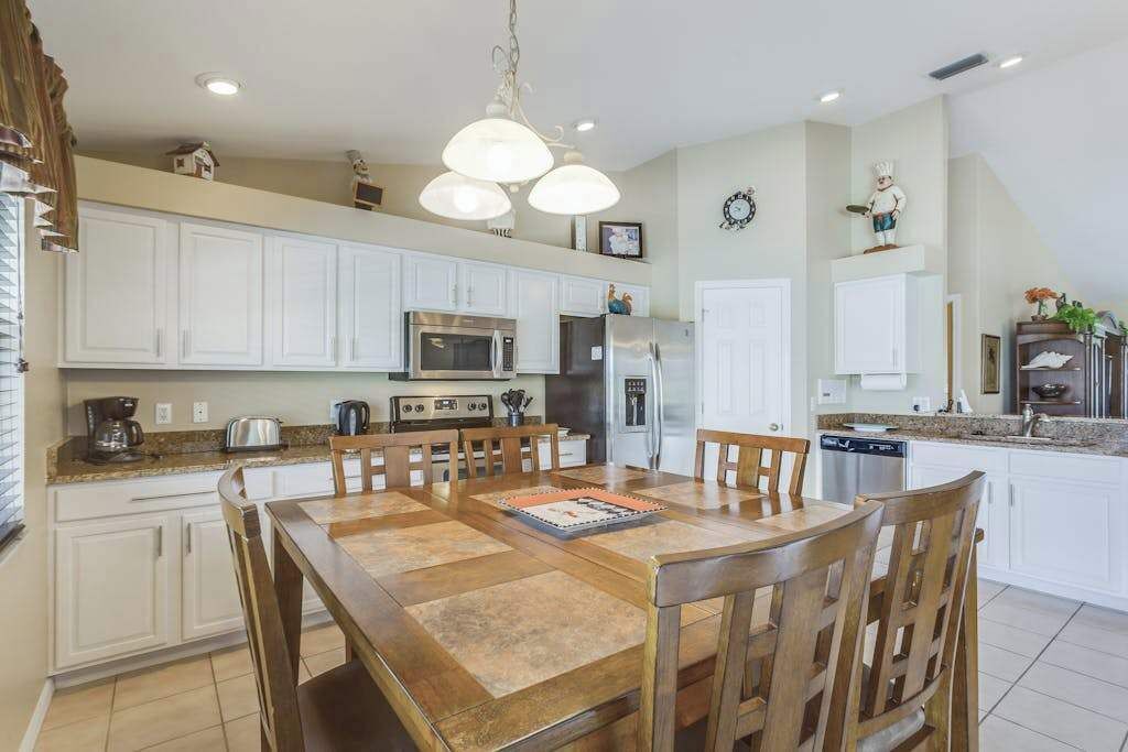Una cocina moderna con armarios blancos, una mesa de comedor con sillas, un microondas, un refrigerador y una cafetera.
