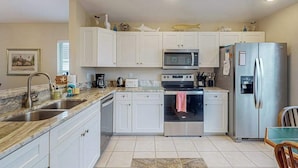 Una cocina con armarios blancos, un refrigerador de acero inoxidable, un microondas, un horno y un lavamanos.