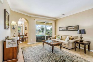 A living room with a sofa, coffee table, and a dining area with chairs. - Spacious home with screened-in pool & lush lakefront views - minutes to beaches (Fort Myers)