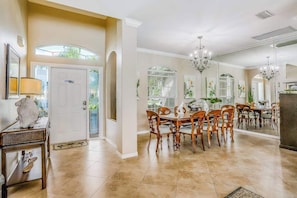 A dining area with a round table and chairs, a chandelier, and a door leading to another room. - Spacious home with screened-in pool & lush lakefront views - minutes to beaches (Fort Myers)
