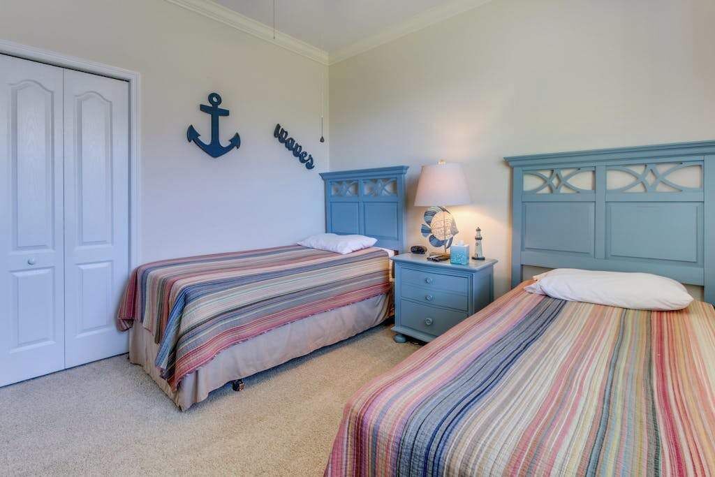 A bedroom with two beds, a nightstand, a lamp, and a wardrobe.