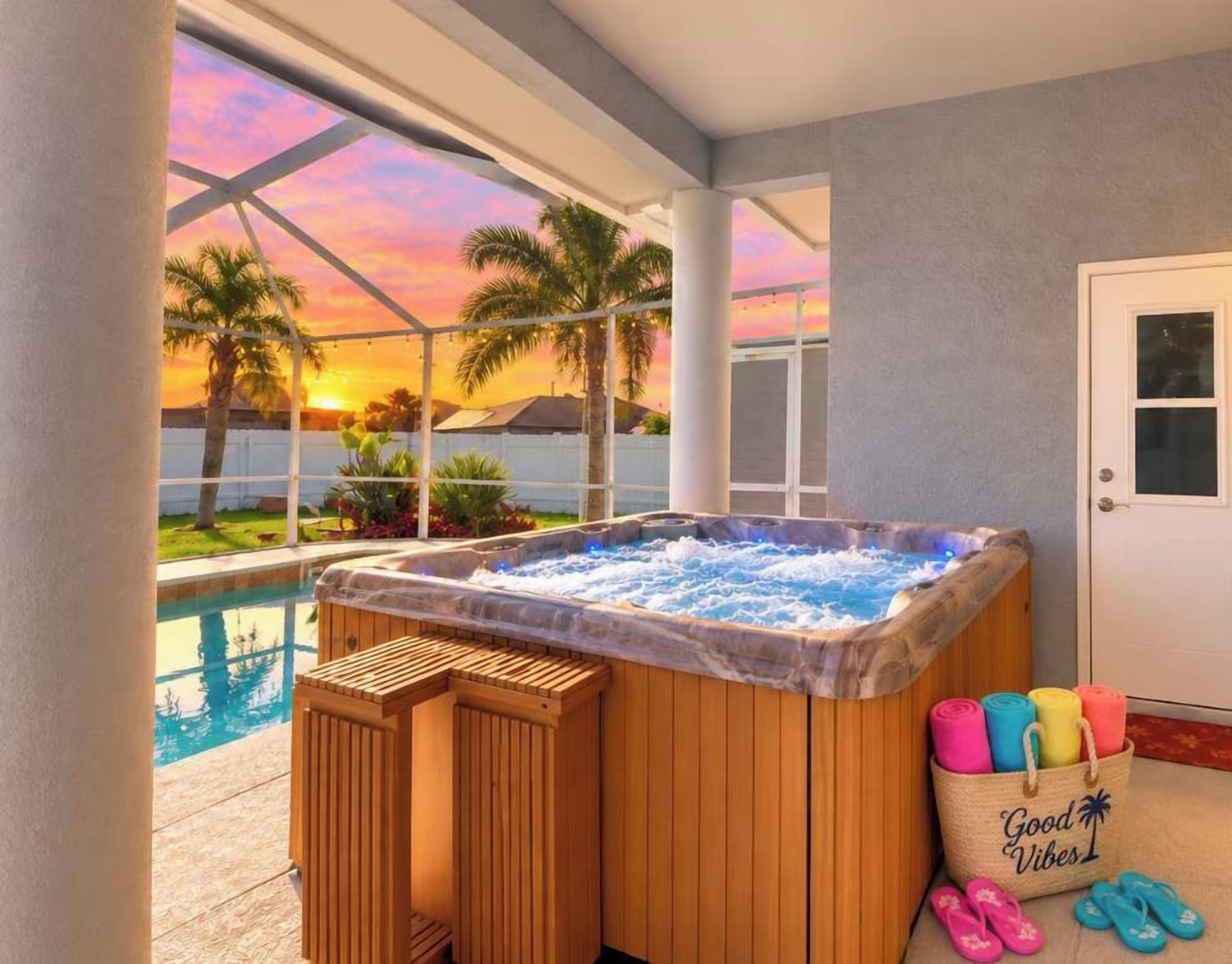 A hot tub with a view of a pool and sunset, wooden deck, and a door with a towel rack.