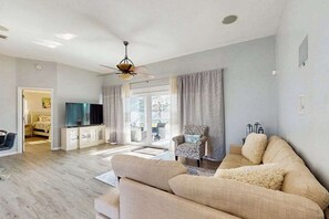 Ein Wohnzimmer mit einer Couch, einem gemusterten Sessel, einem Fernseher und einem Deckenventilator.