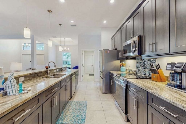 A modern kitchen with dark cabinets, stainless steel appliances, and a marble countertop. - Spacious Canal-Front home with private pool, lanai, Game Room (Cape Coral)