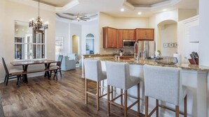 Una cocina moderna con armarios de madera, una isla central con taburetes de bar, una zona de comedor con mesa y sillas, y un ventilador de techo.
