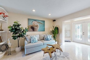 A living room with a sofa, a painting, and a wooden coffee table. - Waterfront home with private pool, lanai, dock, & tiki hut (Cape Coral)