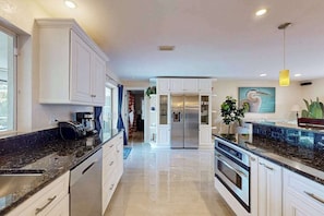 A modern kitchen with white cabinetry, a central island, and a refrigerator. - Waterfront home with private pool, lanai, dock, & tiki hut (Cape Coral)
