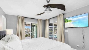 Une chambre avec un lit, un ventilateur de plafond, une télévision et une vue sur une piscine et un espace extérieur.