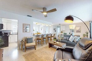 Ein modernes Wohnzimmer mit Sofa, Couchtisch und Sesseln, ein Essbereich mit Tisch und Stühlen sowie eine Küche im Hintergrund.