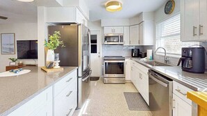 Una cocina moderna con muebles blancos, electrodomésticos de acero inoxidable, un microondas, una cafetera y un reloj en la pared.
