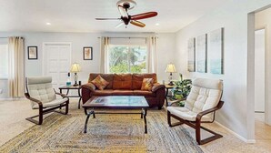 Ein Wohnzimmer mit einem braunen Sofa, zwei Sesseln, einem Couchtisch, einem Deckenventilator und gerahmten Kunstwerken an den Wänden.