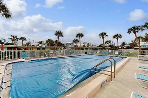 A swimming pool with a blue cover, surrounded by lounge chairs and palm trees. - Canal-front condo with private docks, heated pool, private beach access (Englewood)