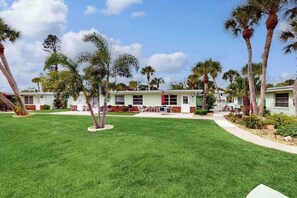 A row of single-story buildings with a well-maintained lawn and palm trees. - Canal-front condo with private docks, heated pool, private beach access (Englewood)