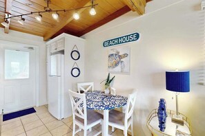 Ein Essbereich mit Tisch, Stühlen, einer Lampe und einem Wandschild mit der Aufschrift 'BEACH HOUSE'.